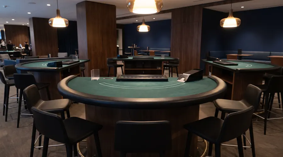 Generated scene: an empty blackjack table with green felt, a closed card shoe and empty stools under pendant lamps; not a photograph of the casino.